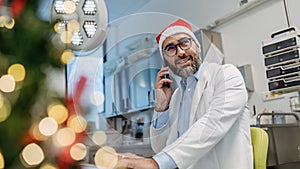Portrait of doctor phone calling in emergency room, decorated for Christmas. Mature male doctor with Santa hat