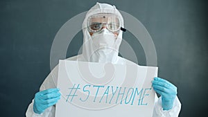 Portrait of doctor in protective clothes holding stayhome banner on grey background