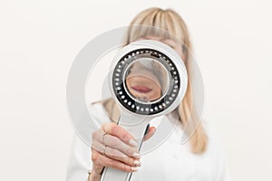 Portrait of a doctor trichologist dermatologist looking at a dermatoscope. Focus on the hand with a dermatoscope, the doctor is