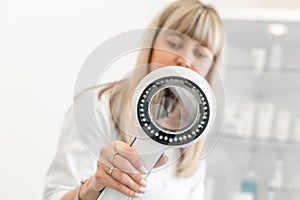 Portrait of a doctor trichologist dermatologist looking at a dermatoscope. Focus on the hand with a dermatoscope, the doctor is