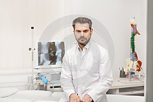 Portrait of doctor in white coat at workplace with medical staff on the background. Male doctor working at office desk