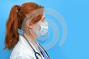 Portrait of a doctor woman in medical mask, closeup. Nurse in a white uniform and a protective mask on a blue background, profile