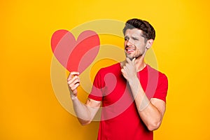 Portrait of doubtful guy celebrate 14-february date get red big paper card heart think disagree dislike wear modern