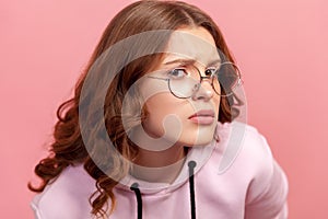 Portrait of doubting young curly haired woman in eyeglasses looking at camera with unsure eyes and furrowed eyebrows, uncertain