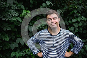 Portrait of down syndrome adult man standing outdoors at green background, looking at camera.