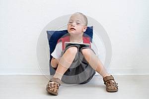 A portrait of down-syndrome school boy sitting on the floor, using tablet.