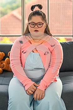 portrait of down syndrome teenager girl sitting on fosa at home