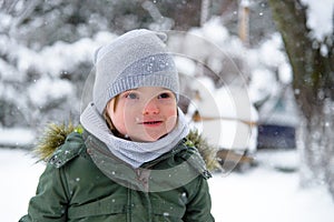 Portrait of Down syndrome toddler boy in a winter outfit, a warm grey scarf in a green jacket enjoys the frosty winter weather