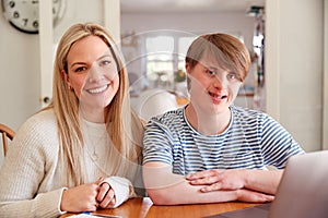 Portrait Of Downs Syndrome Man Sitting With Home Tutor Using Laptop For Lesson At Home photo