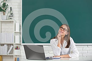 Portrait of dreaming young college student in classroom on blackboard background, copy space.