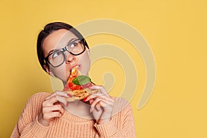 Portrait of dreaming young girl tasting Italian pizza isolated on yellow studio background. World pizza day