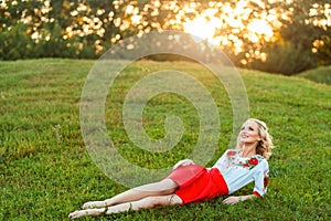 Portrait of dreamy beautiful blonde young woman with curly hairstyle in stylish dress posing with happiness on green grass and