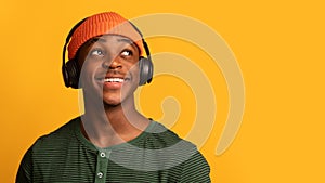 Portrait Of Dreamy Black Hipster Guy Listening Music In Wireless Headphones