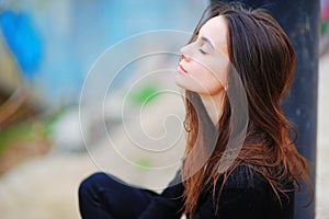 Portrait of a dreamy cute happy woman worker meditating outdoors with big eyes closed, sitting with the effect of blur closeup. De