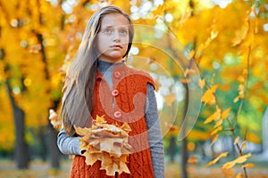 Portrait of dreamy girl in autumn city park. Posing with bouquet of yellow leaves. Bright sunlight and golden trees, fall season