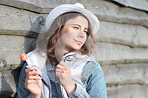 Portrait of dreamy girl with a lollipop near wooden fence. Beautiful young caucasian woman with sweet Chupa-Chups. Spring holidays