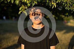 Portrait of dreamy teen boy with eyes closed in garden. Beautiful shadow from the leaves on the face