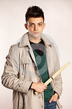 Portrait of a drummer with drum stick wearing a coat and greeen shirt in studio