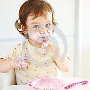 Portrait of eating baby girl with dirty face in high chair