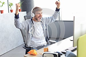 Portrait of ecstatic gamer guy in headphones screaming and rejoicing while playing video games on computer