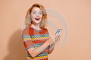 Portrait of ecstatic girl with wavy hairdo wear t-shirt hold smartphone impressed by internet speed isolated on beige