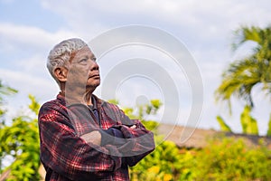 Portrait of an elderly Asian man with gray hair, arms crossed and looking up while standing in a garden. Concept of aged people