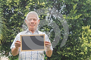 Portrait of an elderly Asian man holding a mini blackboard and looking at the camera while standing in the garden
