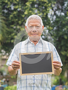 Portrait of an elderly Asian man with short gray hair holding a mini blackboard, smiling and looking at the camera while standing