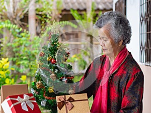 Portrait of elderly Asian woman looking at the Christmas tree while standing at home. Concept of aged people and festivals