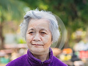 Portrait of elderly Asian woman with short gray hair and standing smiling and looking at the camera while standing in a garden.
