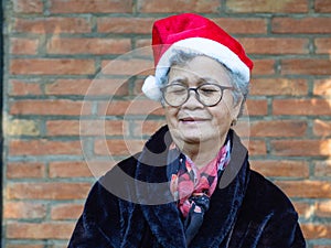 Portrait of an elderly Asian woman wearing a red hat with eyes closed and smiling while standing with brick wall background