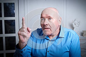 Portrait of an elderly bald man in a blue shirt in the room. A poor pensioner lives alone