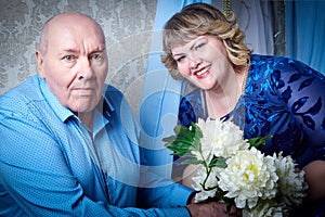 Portrait of an elderly bald man and fat plump woman in a blue dress in a nice room. Old pensioner father and adult daughtes posing