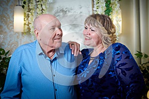 Portrait of an elderly bald man and fat plump woman in a blue dress in a nice room. Old pensioner father and adult daughtes posing