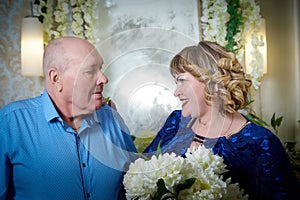 Portrait of an elderly bald man and fat plump woman in a blue dress in a nice room. Old pensioner father and adult daughtes posing