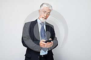 Portrait of elderly businessman in suit holding mobile phone in hand with happy smiling face. Person with smartphone