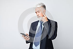 Portrait of elderly businessman in suit looks on mobile phone and thinks. Person with smartphone