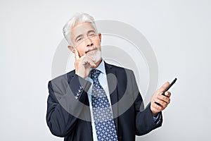 Portrait of elderly businessman in suit looks on mobile phone and thinks. Person with smartphone