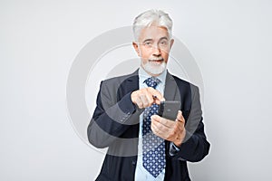 Portrait of elderly businessman in suit showing blank mobile phone screen with excited face. Person with smartphone