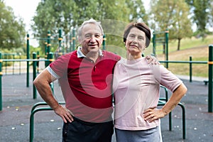 Portrait of an elderly couple in sportswear on sports ground in a city park on summer day