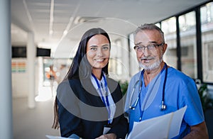 Portrait of elderly doctor and business woman at hospital corridor. photo