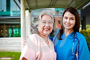 Portrait of an elderly female patient and a surgeon, both smiling brightly, standing outside a building.