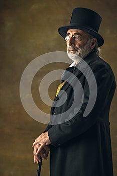 Portrait of elderly gray-haired man, gentleman, aristocrat or actor posing isolated on dark vintage background. Retro