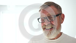 Portrait of an elderly happy pensioner with glasses with a grey beard and a white t-shirt. Happy retirement