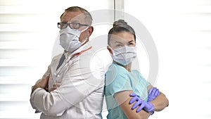 Portrait of an elderly male doctor and a young nurse wearing medical masks showing OK. Professional tandem.