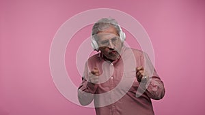 Portrait of an elderly man with glasses is fun dancing and enjoying music in big white headphones. Gray haired pensioner