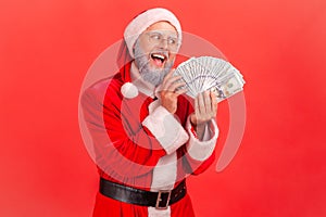 Portrait of elderly man with gray beard wearing santa claus costume with excited expression, greedy