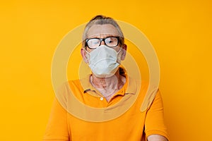 Portrait elderly man medical mask on the face protection close-up yellow background