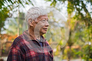 Portrait of an elderly man smiling and looking away while standing in a garden. Space for text. Concept of aged people