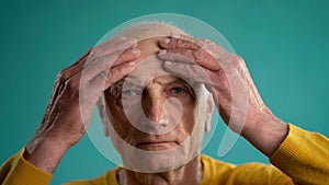 Portrait of an elderly man suffering from headache, old man massaging forehead with two hands